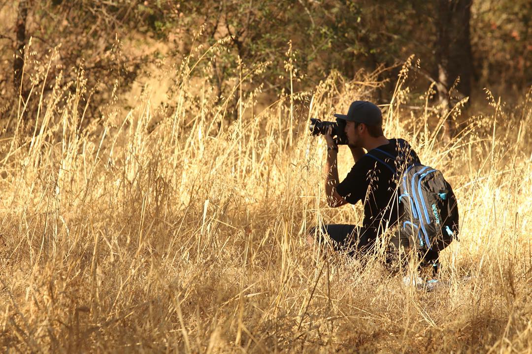Kyle crouched in tall grass shooting in golden light